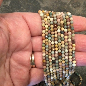 May include: A strand of multi-colored gemstone beads, featuring shades of brown, green, pink, and white. The beads are faceted and have a slightly irregular shape.