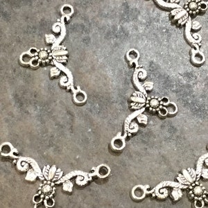 May include: Five silver-toned metal connector charms with a floral design. Each charm has three loops for attaching to jewelry or other crafts.