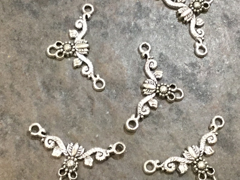 May include: Five silver-toned metal connector charms with a floral design. Each charm has three loops for attaching to jewelry or other crafts.