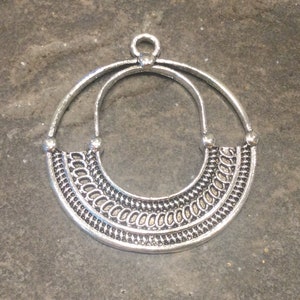 May include: Silver-toned metal pendant with a circular design. The pendant features a half-moon shape with intricate patterns and a loop at the top for hanging. The design is symmetrical and detailed, suitable for jewelry making.