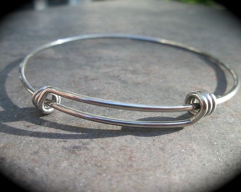 May include: A silver expandable bangle bracelet with a knotted closure.