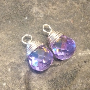 May include: A pair of earrings with purple faceted gemstone drops wrapped in silver wire.