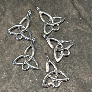 May include: Six silver Celtic knot charms, each featuring a three-dimensional design with a loop at the top for attaching to jewelry or other crafts.