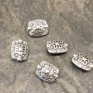 May include: Five silver-toned metal beads with an ornate design. The beads are rectangular in shape and have a raised, intricate pattern.