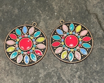 May include: Two round metal pendants with a colorful enamel design. The pendants feature a central red circle surrounded by a ring of smaller multi-colored circles and a ring of leaf-shaped designs in pink, blue, green, and yellow.
