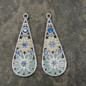 May include: A pair of silver teardrop-shaped earrings with a floral design. The flowers are light blue and yellow with blue rhinestones in the center.