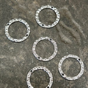 May include: Five silver metal rings with a textured surface. The rings are all the same size and shape, and they have a hole in the center.