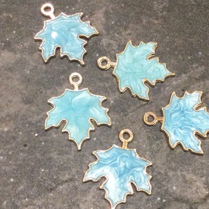 May include: Five gold-toned metal maple leaf charms with a light blue enamel finish. Each charm has a loop at the top for attaching to jewelry or other crafts.