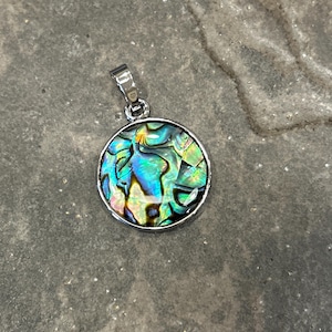 May include: A silver pendant with a round abalone shell inlay. The shell has a swirling pattern of green, blue, and gold.