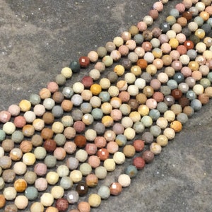 May include: A strand of multi-colored gemstone beads. The beads are faceted and have a variety of colors, including brown, tan, pink, and green. The beads are strung on a clear thread.