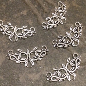 May include: Five silver metal decorative charms in the shape of a vine with leaves. Each charm has two loops at the top for attaching to jewelry or other crafts.