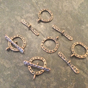 May include: A set of eight antique copper-toned metal clasps with a hammered finish. Each clasp features a round ring and a straight bar.