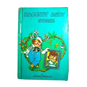 May include: Vintage "Raggedy Andy Stories" book with a teal cover. The cover features a cartoon illustration of Raggedy Andy holding a framed picture of Raggedy Ann, surrounded by a floral wreath and small fairy-like figures. The author's name, Johnny Gruelle, is at the bottom.