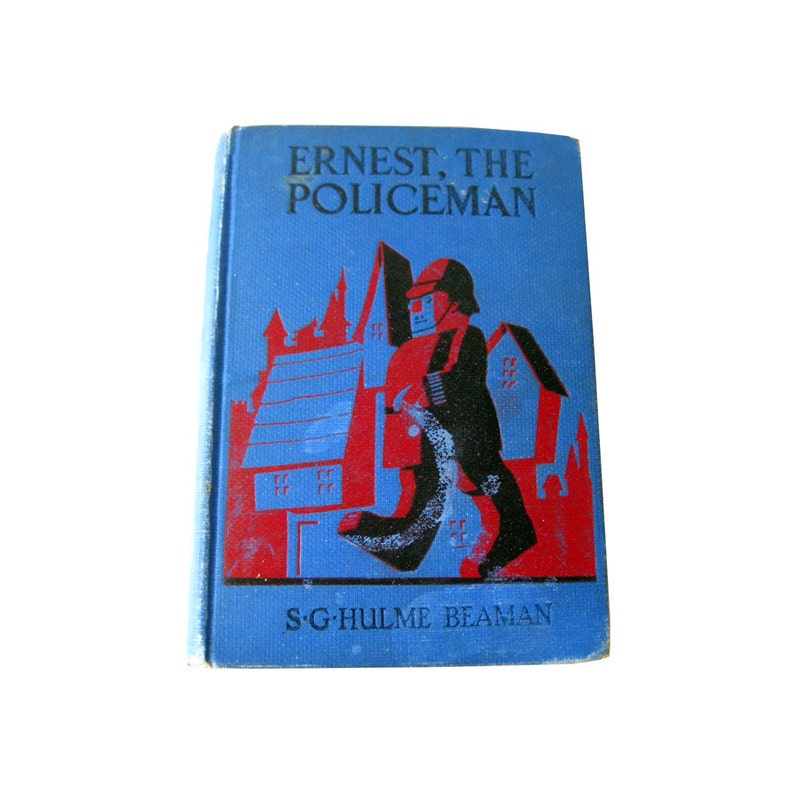 May include: A vintage book titled "Ernest, The Policeman" with a blue cover. The cover features a red and black illustration of a policeman walking past red buildings. The author's name, S.G. Hulme Beaman, is printed at the bottom.