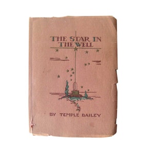 May include: A vintage book titled "The Star in the Well" by Temple Bailey. The cover is a faded pink with green and brown illustrations of a well, stars, and trees. The book shows signs of wear.