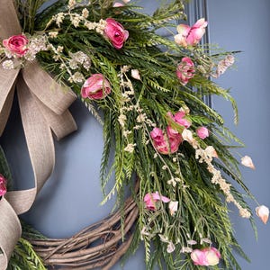 K&ouml;nnte beinhalten: Ein rosafarbener und gr&uuml;ner Blumenkranz mit einer Schleife aus Sackleinen. Der Kranz ist aus Weinreben gefertigt und hat rosafarbene Bl&uuml;ten und gr&uuml;ne Bl&auml;tter.