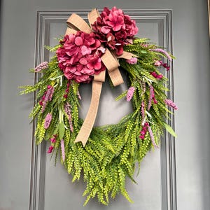 Corona de hortensias rosas: follaje en cascada, lazo de arpillera y decoración de parra.