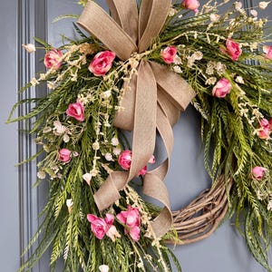 K&ouml;nnte beinhalten: Ein Fr&uuml;hlingskranz mit einer Schleife aus Sackleinen und rosa Bl&uuml;ten. Der Kranz ist aus Weide und hat ein kaskadierendes Design.