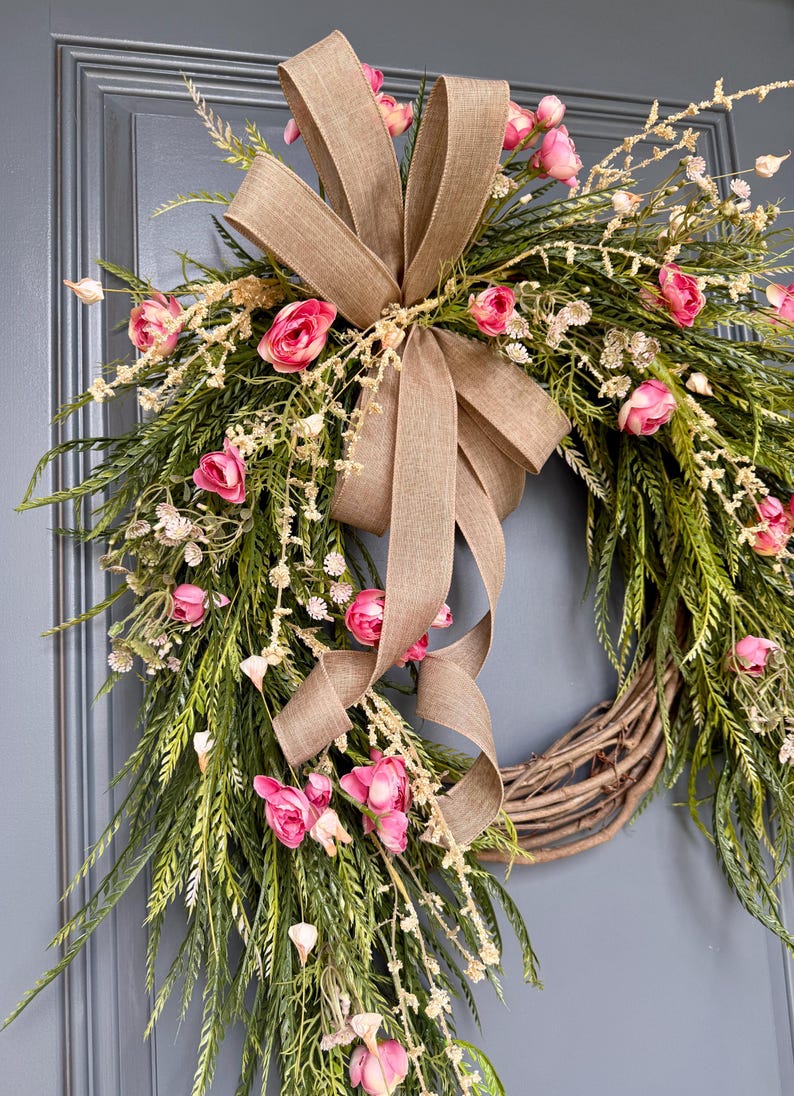 K&ouml;nnte beinhalten: Ein Fr&uuml;hlingskranz mit einer Schleife aus Sackleinen und rosa Bl&uuml;ten. Der Kranz ist aus Weide und hat ein kaskadierendes Design.