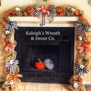 May include: A fireplace mantel decorated with a fall-themed garland. The garland is made of burlap mesh, pumpkins, and fall leaves. Black and white checkered bows and small white pumpkins are also included. The text "Kaleigh's Wreath & Decor Co." is visible.