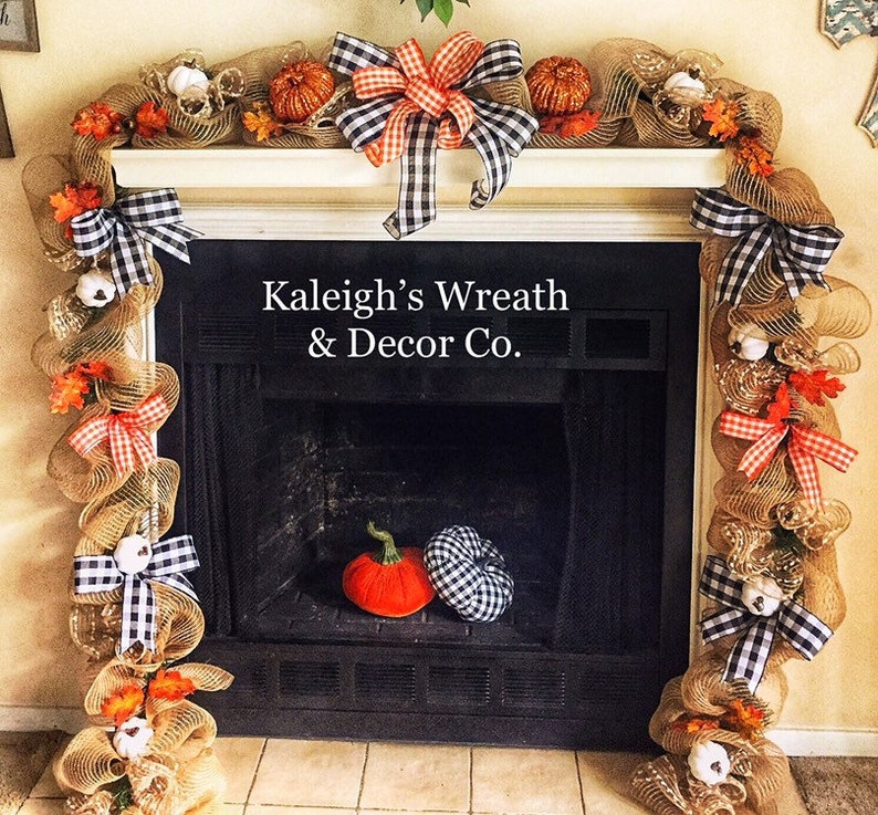 May include: A fireplace mantel decorated with a fall-themed garland. The garland is made of burlap mesh, pumpkins, and fall leaves. Black and white checkered bows and small white pumpkins are also included. The text "Kaleigh's Wreath & Decor Co." is visible.