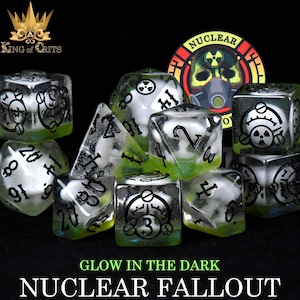 May include: Set of seven clear, glow-in-the-dark dice with black and white markings. The dice feature a skull and crossbones symbol with a radiation symbol. The dice are labeled with numbers 1 through 6. The dice are on a black background. The text "NUCLEAR FALLOUT" is at the bottom of the image.