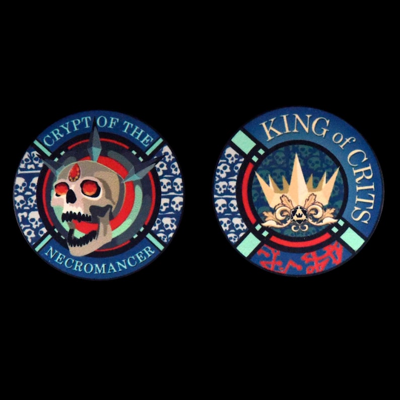 May include: Two round tokens with a black background. One token features a skull with the text "CRYPT OF THE NECROMANCER". The other token has a gold crown and the text "KING of CRITS". Both tokens have a blue, red, and green color scheme.