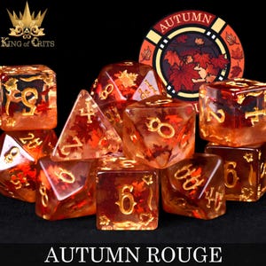 May include: Set of nine translucent dice with gold numbers and autumn leaf inclusions. The dice are in shades of orange and red, with a clear resin base. The dice are arranged in a circle, with a small card in the center that says "Autumn".