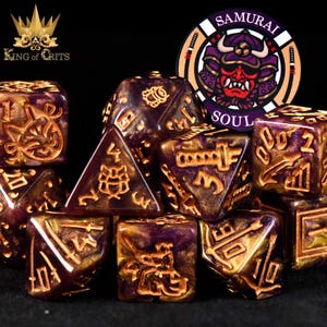 May include: A collection of purple and gold dice with intricate designs and symbols. The dice are arranged in a group, with a logo that says "King of Crits" and a circular emblem that says "Samurai Soul".