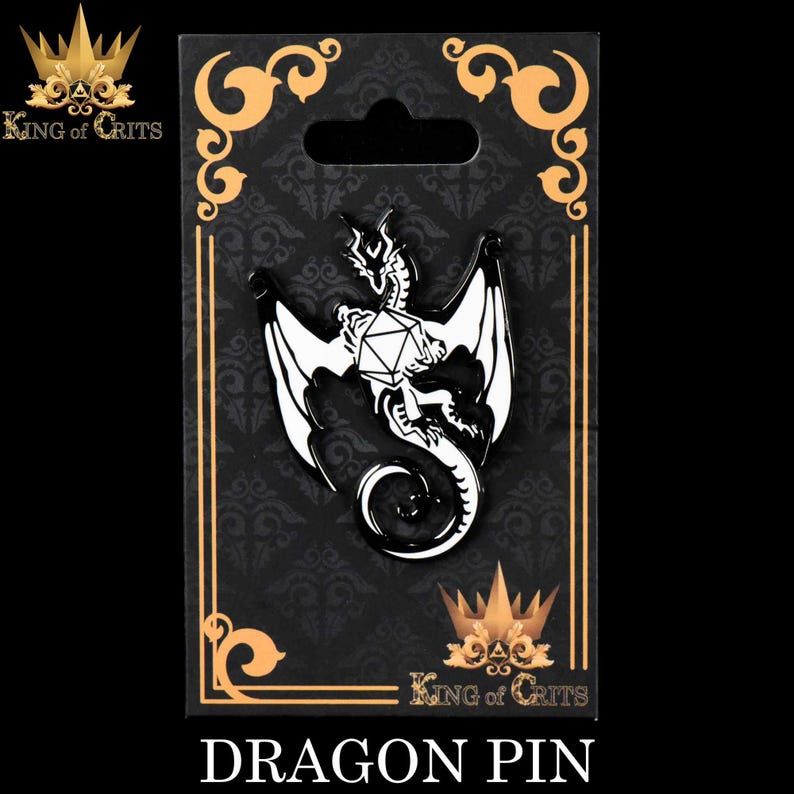 May include: A black and white enamel pin featuring a dragon curled around a white twenty-sided die. The pin is on a black background with gold trim and the text "King of Crits" in gold letters. The text "Dragon Pin" is below the image.