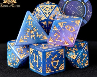 May include: A set of seven polyhedral dice with a blue and purple galaxy-themed design. The dice have gold accents and are decorated with stars and constellations. The dice are labeled with the word "GUIDING" on one of the dice.