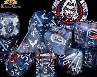 Könnte beinhalten: Eine Sammlung von Würfeln mit einem gotischen Thema. Die Würfel sind hauptsächlich blau mit silbernen Zahlen und Akzenten sowie roten Einschlüssen. Ein Pokerchip mit einer Vampir-Illustration und dem Text "VAMPIRIC LOODLIN" ist ebenfalls vorhanden. Das King of Crits-Logo befindet sich oben links.