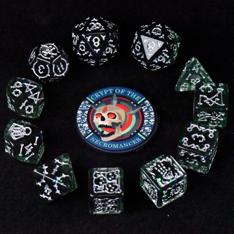 May include: A collection of dice and a circular patch with a skull design. The dice are black and green with white markings, including skulls and bones. The patch reads "Crypt of the Necromancer" with a skull in the center.