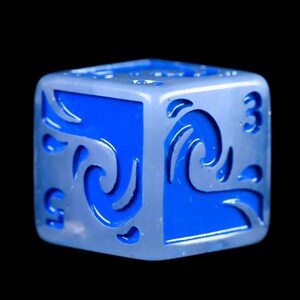 Puede incluir: Un dado plateado y azul de seis caras con un dise&ntilde;o de olas. El dado tiene un interior azul con recortes de olas plateadas y n&uacute;meros blancos. Los n&uacute;meros 3 y 5 son visibles en el dado.