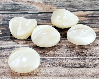 May include: Five white, pearlescent, round buttons with a slightly irregular shape. The buttons have a smooth, glossy finish and are arranged on a wooden surface.