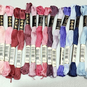 May include: A collection of 30 embroidery floss spools in various shades of pink, red, purple, blue, and grey. Each spool has a black label with white text.