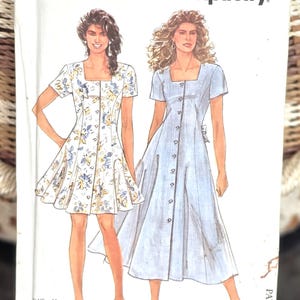 May include: Simplicity sewing pattern featuring two dress designs. The pattern packet has the text "It's SO EASY" and "it's Simplicity." The size range is 8-20. One dress is white with a floral print, and the other is a light blue button-down dress.