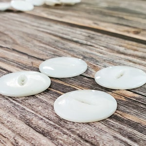 May include: Four white oval buttons with two holes each, arranged on a wooden surface.