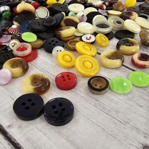 以下が含まれることがあります： さまざまなサイズ、形、色のボタンのコレクション。ボタンには、黒、白、黄色、赤、茶色が含まれます。一部のボタンには2つの穴があり、他のボタンには4つの穴があります。ボタンは明るい色の木製の表面に散らばっています。