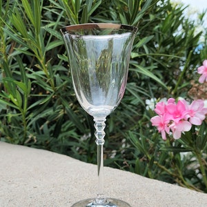 May include: A clear glass wine glass with a silver rim. The glass has a delicate stem with a textured design. The glass is sitting on a gray surface.