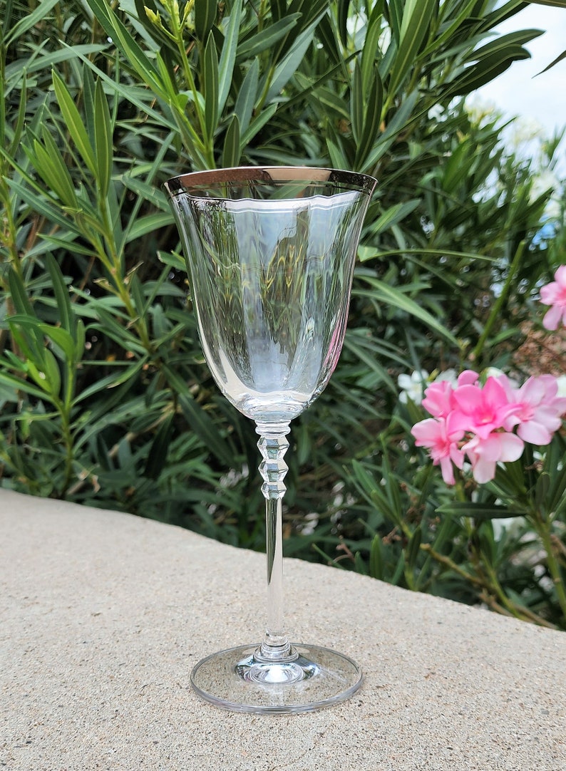 May include: A clear glass wine glass with a silver rim. The glass has a delicate stem with a textured design. The glass is sitting on a gray surface.