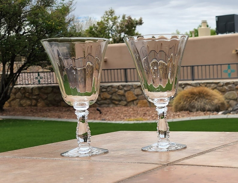 May include: Two clear glass wine glasses with a beaded stem and a fluted bowl.