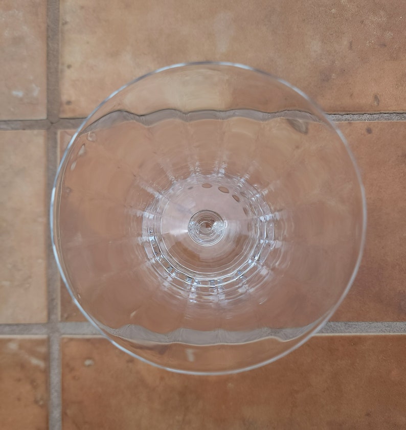 May include: A clear glass wine goblet with a fluted design. The goblet is empty and has a round base.
