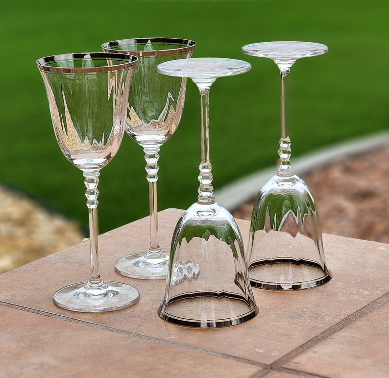 May include: Four clear glass wine glasses with a stemmed base. Three of the glasses are standard wine glasses, and one is a bell-shaped glass.