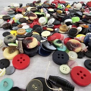 以下が含まれることがあります： さまざまな色、形、サイズのボタンのコレクション。赤、黒、白、黄色、青のボタンが含まれており、一部は2つまたは4つの穴があります。ユニークなデザインとテクスチャのボタンもあります。