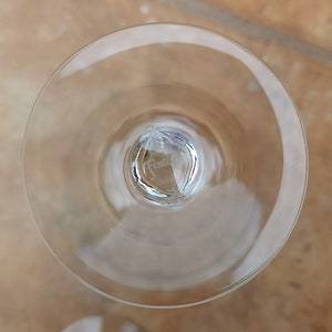 May include: The underside of a clear glass wine glass with a small, round, clear glass base. The base has the word "Fosta" etched into it.