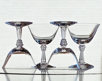 May include: Four clear glass cocktail glasses with a stemmed base and a wide bowl. The glasses are arranged in a row, with the bowls overlapping.