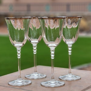 May include: Four clear glass wine glasses with silver rims sit on a brown surface. The glasses are empty and have a stemmed base.