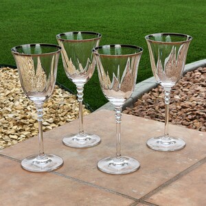 May include: Four clear glass wine glasses with silver rims. The glasses are arranged in a row on a brown tiled surface.