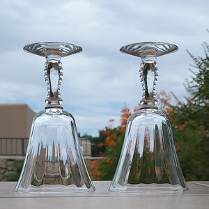 May include: Two clear glass bell-shaped drinking glasses with a beaded stem and a fluted design.
